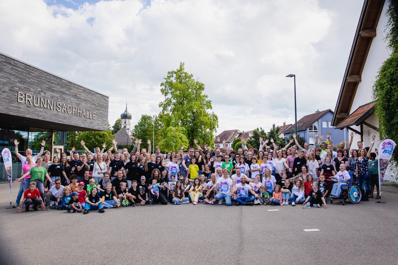 Kinder, Familien und das Team der Superheldenschmiede lächeln gemeinsam in die Kamera